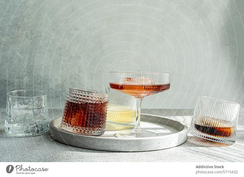 Eine Auswahl an alkoholischen Getränken in strukturierten Gläsern, elegant präsentiert auf einem runden Betontablett mit einem weichen grauen Hintergrund