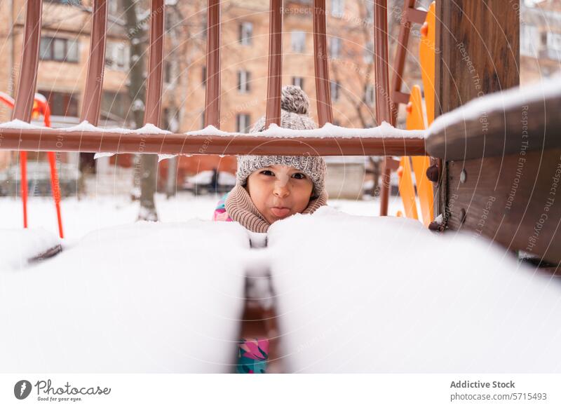 Neugieriges Kind späht in Winterkleidung durch verschneite Spielgeräte guckend Schnee Spielplatz Kleidung neugierig im Freien kalt spielen Gerät Schal