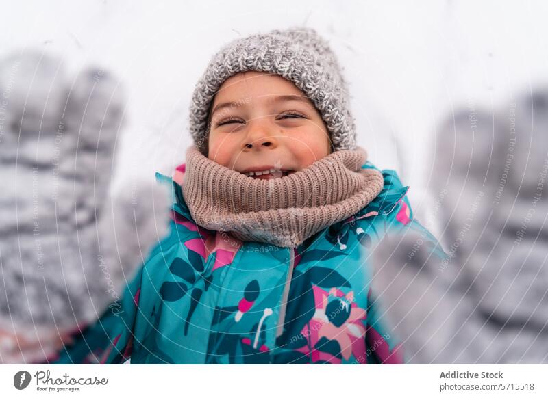 Glückliches Kind mit erhobenen Fäustlingen, lächelnd in einer verschneiten Winterlandschaft Fausthandschuh Lächeln Schnee im Freien Freude Schal kalt