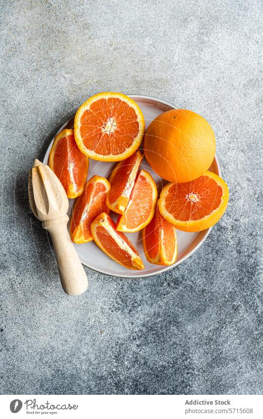 Frisch geschnittene Orangen auf einem Teller mit einer hölzernen Saftpresse orange Zitrusfrüchte Frucht Scheibe Entsafter frisch ganz Keramik grau Oberfläche
