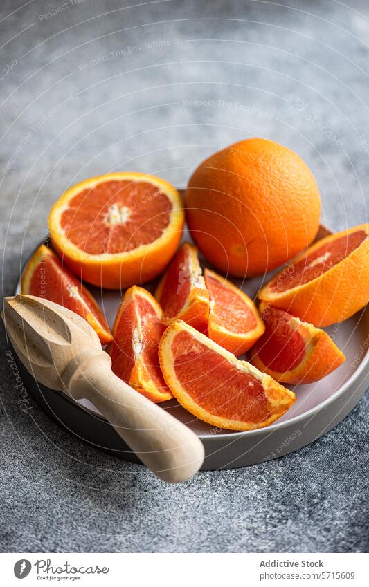 Frisch geschnittene Orangen auf einem Teller mit einer hölzernen Saftpresse Frucht orange aufgeschnitten Entsafter Zitrusfrüchte reif frisch grau Hintergrund