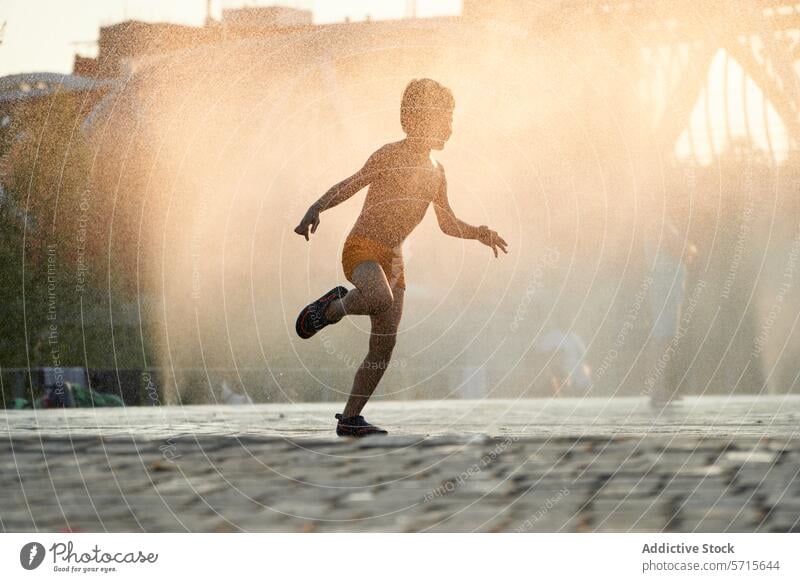 Im warmen Licht des Sonnenuntergangs tanzt ein fröhliches Kind im Wassernebel eines städtischen Brunnens und verkörpert so den Geist des Sommers. urban