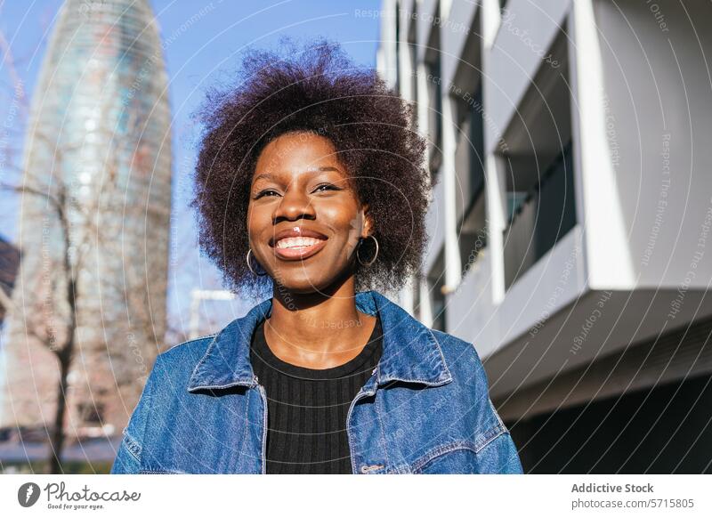 Eine strahlende afroamerikanische Frau mit einem selbstbewussten Lächeln steht in einer städtischen Landschaft, die Architektur der Stadt umrahmt ihre natürliche Schönheit