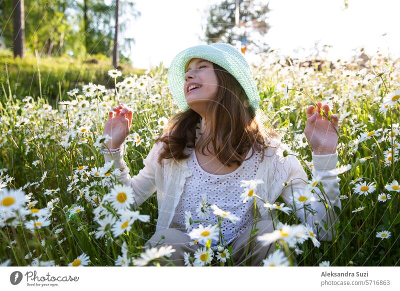 Mädchen sitzt auf einer Wiese mit Wildblumen. Hintergrund des Feldes mit blühenden Gänseblümchen. Sonniger Sommertag, Strahlen des Lichts. Sommerurlaub Konzept