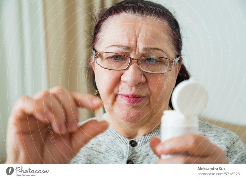 Ältere Frau, die Medikamente einnimmt, Pille in der Hand hält und durch eine Brille schaut. Ältere Person mit besorgtem Gesicht, die das Rezept auf der Medikamentenflasche liest.