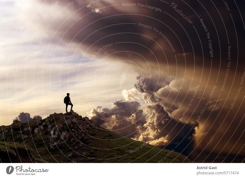 Ein Mann steht auf einem Berg und schaut in eine fantastische Wolkenlandschaft gebirge berg mann bergsteiger gipfel himmel wolken wolkengebilde sonnenuntergang