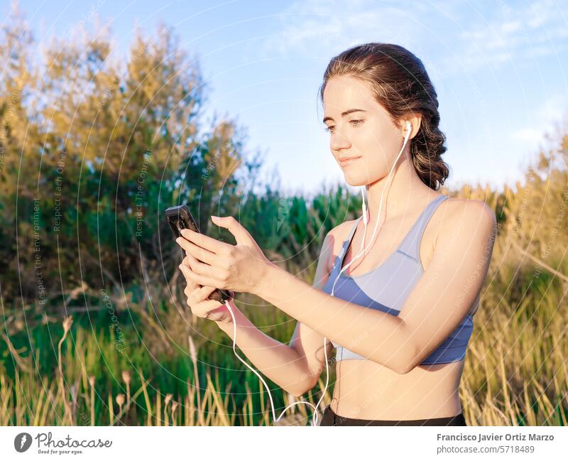 Frau in Sportkleidung schaut im Park auf ihr Mobiltelefon Telefon Fitness Übung Straße Sonnenuntergang Technik & Technologie Gesundheit Athlet Großstadt