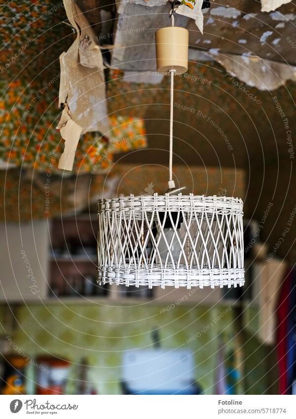Eine Lampe aus Rattan oder so hängt zwischen sich lösender Tapete mit wildem Muster, die in Fetzen von der Decke hängt. Rattan-Lampen Möbel Design Stil rustikal