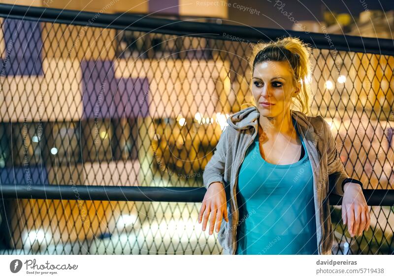 Porträt einer Sportlerin in legerer Sportkleidung, die sich nachts in einer städtischen Umgebung über einem Geländer ausruht Athlet Frau aussruhen Nacht urban