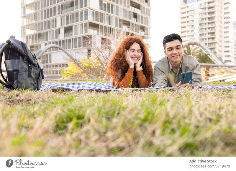 Junges Paar genießt ein Picknick im Stadtpark Mann Frau Smartphone Großstadt im Freien Decke Gras Gebäude Lächeln Freizeit Erholung Glück lässig Konnektivität