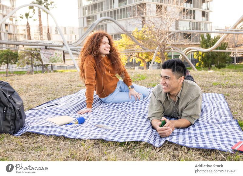 Lachende Schüler genießen ein Picknick in einem Park. lachen Decke multiethnisch Mann Frau Rucksack Wasserflasche Buch Gras im Freien Freizeit Erholung