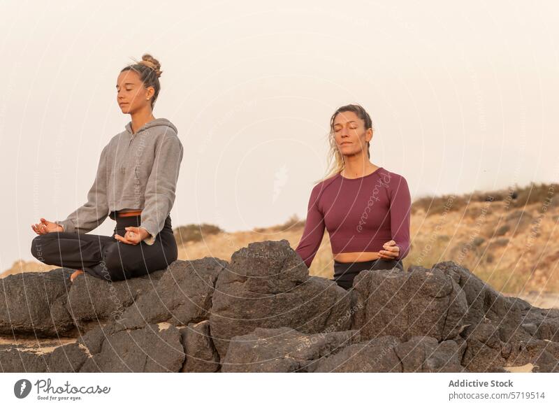 Gelassene weibliche Yoga-Praktizierende meditieren am Strand bei Sonnenuntergang Meditation Gelassenheit üben Achtsamkeit Frieden sitzend einzeln Felsen Himmel