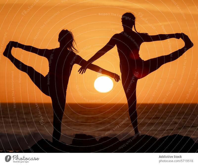 Silhouettiertes Yoga-Duett bei Sonnenuntergang am Strand Silhouette Frauen Gleichgewicht Harmonie Pose Gesundheit Wohlbefinden Lifestyle Fitness Übung Ruhe