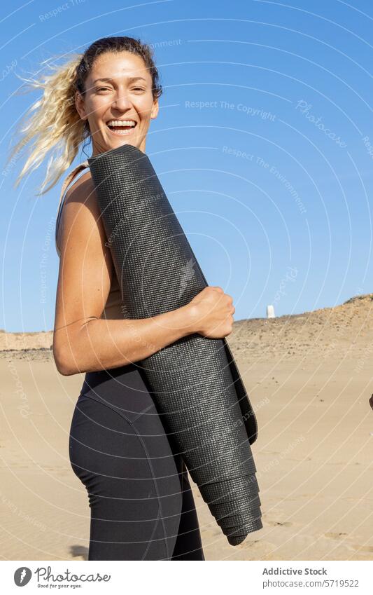 Lächelnde Frau mit Yogamatte am Strand Unterlage Gesundheit aktiv Fitness sonnig im Freien Lifestyle Übung Wellness freudig aktive Kleidung Sport Sand Freizeit