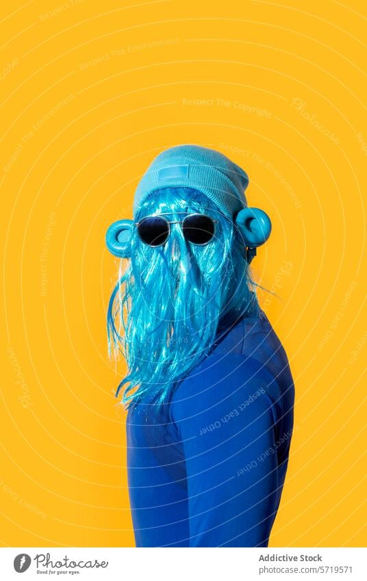 Exzentrische blaue Perücke und Sonnenbrille auf gelbem Hintergrund Person Rücken Kopfhörer farbenfroh schrullig hell lebhaft Pop Kultur Mode exzentrisch Tracht