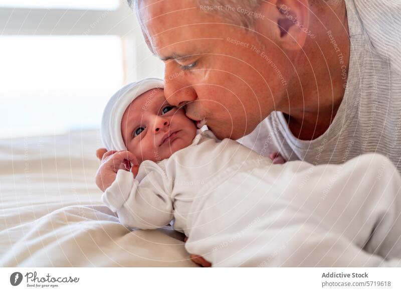 Ein Vater küsst liebevoll die Stirn seines Neugeborenen, während das Baby es mit großen Augen ansieht - ein herzerwärmender Familienmoment Küssen neugeboren