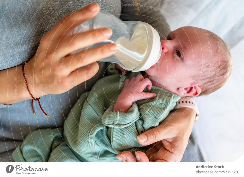 Ein Neugeborenes liegt bequem in den Armen einer anonymen Mutter und wird mit einer Milchflasche gefüttert, was einen nährenden und fürsorglichen Moment darstellt.