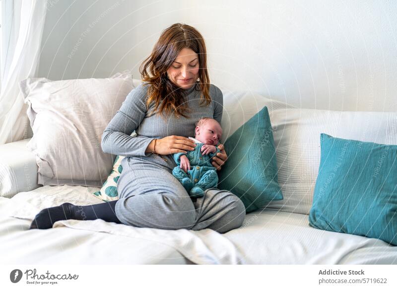 Eine ruhige Mutter sitzt auf einem Sofa und kuschelt sich an ihr neugeborenes Baby, umgeben von bequemen Kissen in einem hellen Raum Kuscheln Kopfkissen