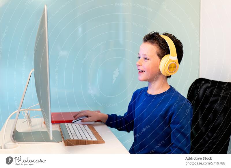 Ein fröhliches Kind interagiert mit einem Computer, trägt leuchtend gelbe Kopfhörer und zeigt mit einem Lächeln an, dass es Freude an der Aufgabe hat oder erfolgreich ist.