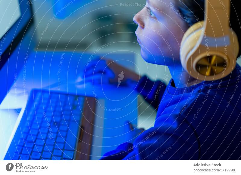 Ein Kind ist mit Kopfhörern in einem abgedunkelten Raum, der vom Licht des Bildschirms erhellt wird, ganz auf den leuchtenden Computerbildschirm konzentriert