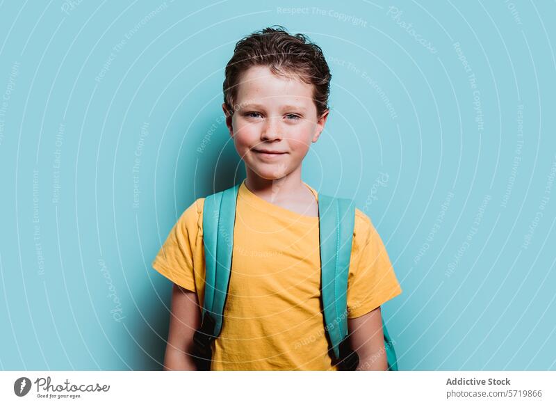 Ein fröhlicher Junge mit einem Rucksack lächelt vor einem türkisfarbenen Hintergrund und strahlt Zuversicht und Vorfreude auf die Schule aus. Lächeln