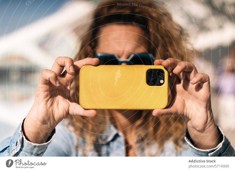 Eine Person mit markanten Händen, denen die Daumen fehlen, hält einen Moment mit einem Smartphone mit gelber Hülle fest; der Fokus der Kamera liegt auf dem angepassten Griff