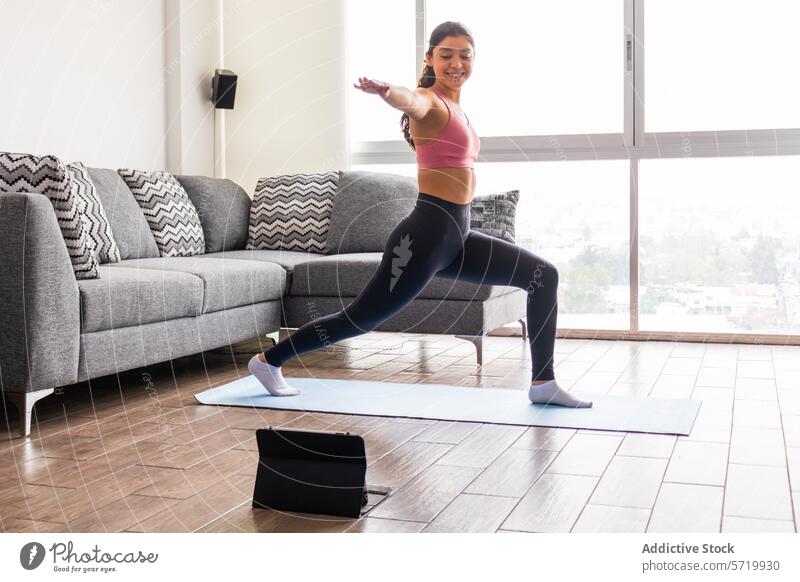 Junge Frau übt die Krieger-II-Pose in Innenräumen online mit Tablette jung Erwachsener hispanisch Krieger-ii-Pose virabhadrasana ii im Innenbereich Yoga Sitzung