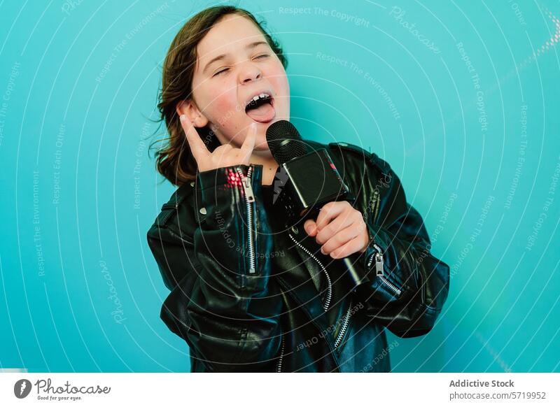 Ein temperamentvolles junges Mädchen mit Rockstar-Attitüde singt vor einem hellblauen Hintergrund in ein Mikrofon und zeigt dabei ein Rockschild. Kind Gesang