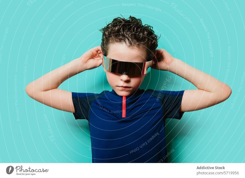 Ein trendiger junger Mann steht selbstbewusst mit den Händen hinter dem Kopf und einem futuristischen Visier vor einem türkisfarbenen Hintergrund. Kind cool