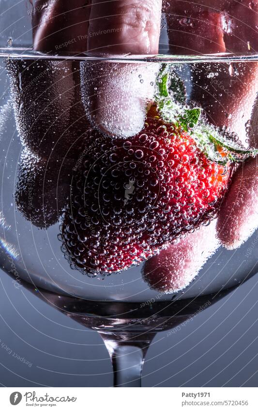 Hand fischt eine frische Erdbeere aus einem Glas. Nahaufnahme. Foodfotografie Ernährung Obst Luftblasen Frucht Lebensmittel flüssig rot food Konzept Kohlensäure