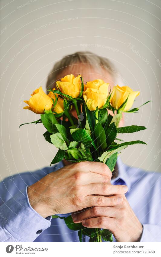 Ein Mann hält einen gelben Rosenstrauß vor sein Gesicht. Blumenstrauß Hände halten Geschenk Frühling Valentinsgruß romantisch Liebe Pflanze Natur Blüte Date