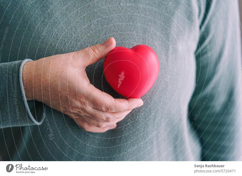 Eine Frau hält ein rotes Herz vor den Oberkörper herzförmig brustkrebs Symbole & Metaphern Gesundheit Vorsorge Liebe Gefühle Zeichen Partnerschaft Treue Glück
