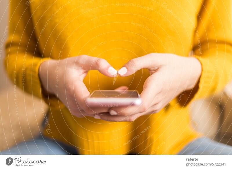 Nahaufnahme von Händen, die eine SMS auf einem Smartphone schreiben. Texten Herzform gelber Pullover Mitteilung digital Konnektivität Zuneigung