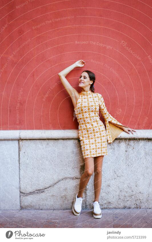 Stilvolle Frau mit erhobenem Arm, die sich auf der Straße an eine Mauer lehnt Model trendy fettarm Wand Arm angehoben retro Außenseite urban Outfit jung feminin