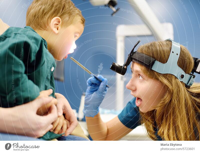 Ein niedlicher kleiner Junge und seine Mutter haben einen Termin bei einem pädiatrischen HNO-Arzt. Der HNO-Arzt untersucht den Rachen des kleinen Patienten mit einem Inspektionsspatel