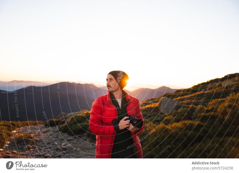 Fotograf fängt Sonnenuntergang in Berglandschaft ein Berge u. Gebirge Landschaft Fotokamera Mann rote Jacke Beanie Hintergrundbeleuchtung Sonnenstrahlen