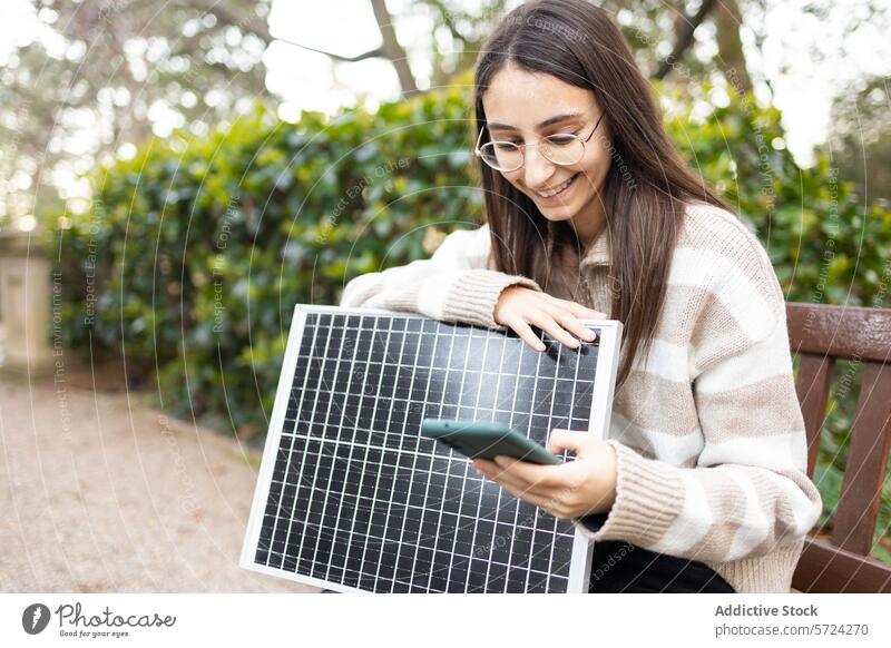 Junge Frau lernt in einem Park über Solarzellen Sonnenkollektor Smartphone Bank Erneuerbare Energie Bildung Lächeln im Freien jung Erwachsener