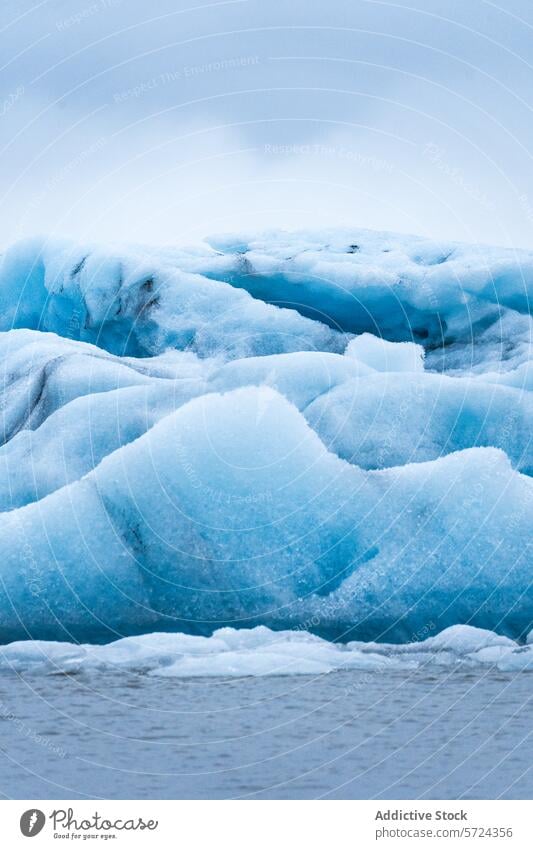 Ein ruhiges Bild, das die subtilen Blautöne eines schwimmenden Eisbergs im Vatnajökull-Nationalpark in Island vor einem sanften grauen Himmel einfängt blau
