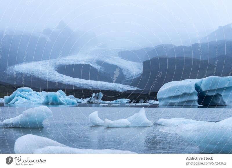 Eisberge treiben in den stillen Gewässern einer Gletscherlagune mit dem in Nebel gehüllten Inlandeis des Vatnajökull und fangen die himmlische Schönheit Islands ein