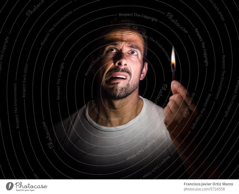 Besorgter Mann mit einem Streichholz in der Dunkelheit. Blackout-Konzept. Gesicht Filmriss Elektrizität Flamme Hand Licht beunruhigt Nacht verwirrt gestresst