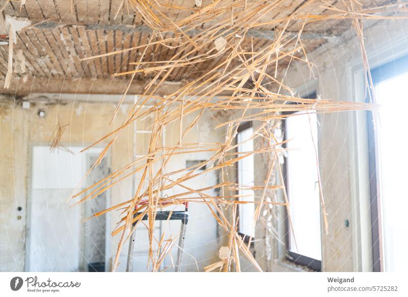 Baustelle Wohnraum mit kahlen Wänden und Holzdecke, von der sich die Strohdämmung wie ein abstraktes Netz Kunstwerk von oben nach unten durchs Bild zieht Abriss