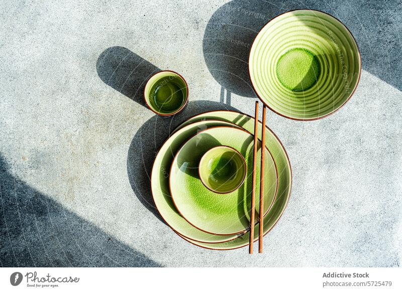 Draufsicht auf ein elegantes grünes Keramik-Tischset im Sonnenlicht von oben Tabelleneinstellung Speise Schalen & Schüsseln Tasse Essstäbchen Schatten Textur