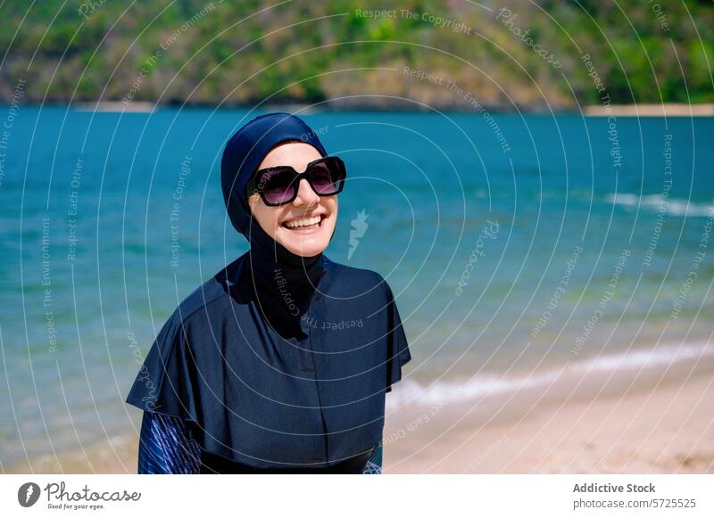 Lächelnde Frau im Burkini genießt den Strand burkini Sonnenbrille muslimisch Badebekleidung Bescheidenheit Mode Sommer sonnig Küste Seeküste Glück Genuss Sand