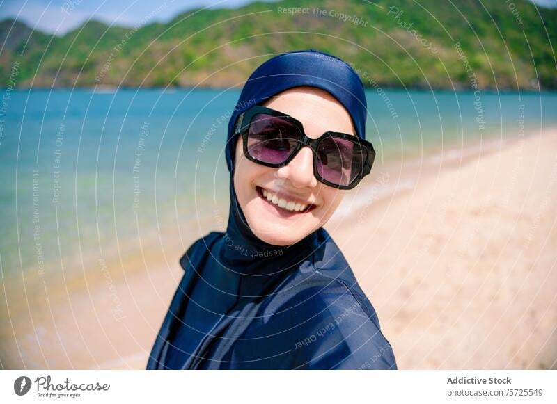 Lächelnde Frau in einem Burkini am Strand burkini bescheidene Bademode Sonnenbad Sand Sonnenbrille Fröhlichkeit Meer Seeküste Küstenstreifen muslimisch
