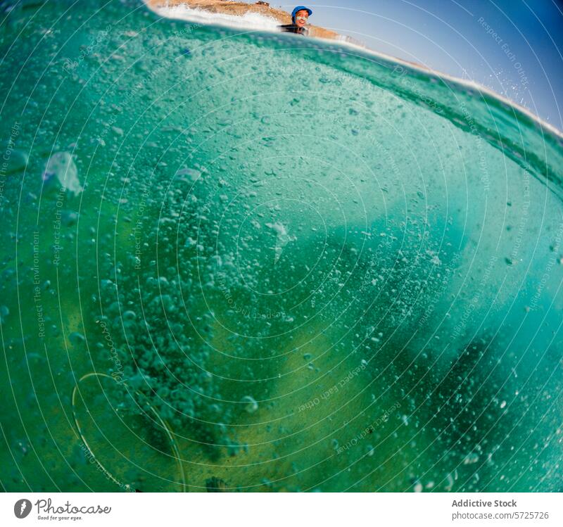 Die Perspektive eines Surfers, umgeben von den intensiven Türkistönen und den sprudelnden Strukturen des Wellenkörpers, unter einem klaren Himmel winken Lauf