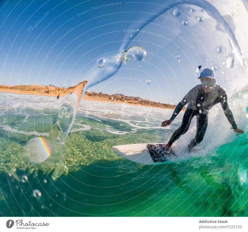 Actiongeladenes Bild eines fokussierten Surfers im Neoprenanzug, der durch eine sich auftürmende Welle schneidet, wobei Wassertropfen um ihn herum schweben