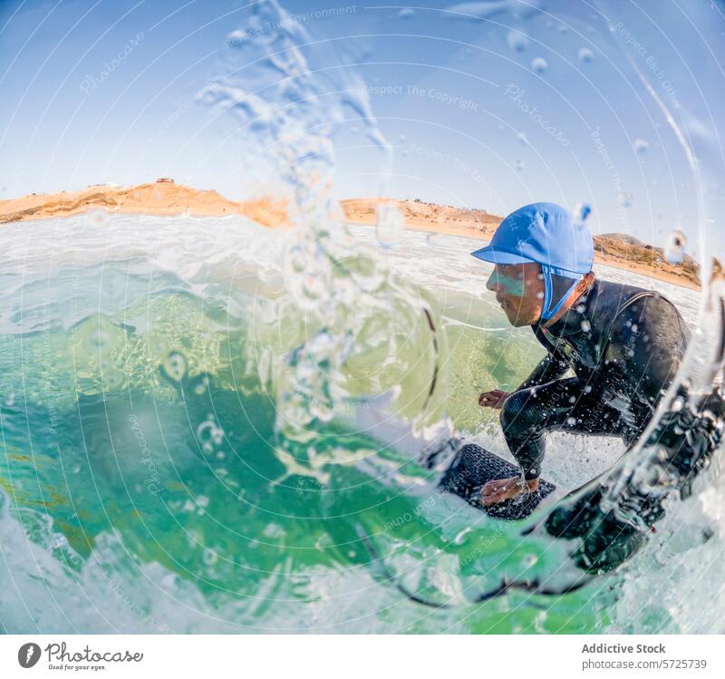 Dynamische Aufnahme eines Surfers im Neoprenanzug, der auf einer grünen Welle reitet, gesehen durch einen Vorhang aus glitzernden Wassertropfen, unter einem blauen Himmel