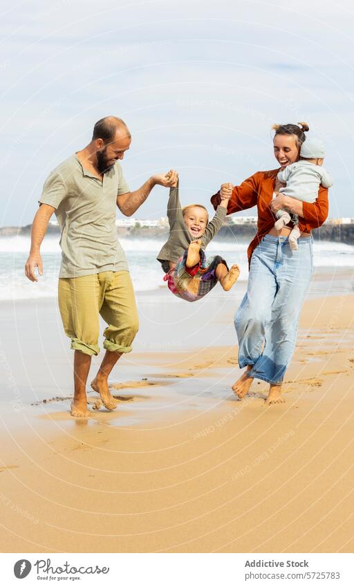 Fröhlicher Familienmoment an einem Sandstrand Strand Spaß spielerisch Freude Fröhlichkeit sonnig Tag Erwachsene Kind swinging Waffen im Freien Freizeit
