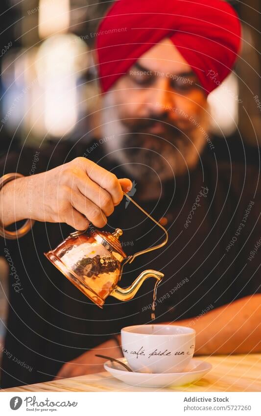 Mann mit rotem Turban gießt Tee in eine Tasse Gießen kupfer Teekanne weiß hölzern Tisch Getränk trinken Tradition Kultur dienen Gastfreundschaft Café Fokus