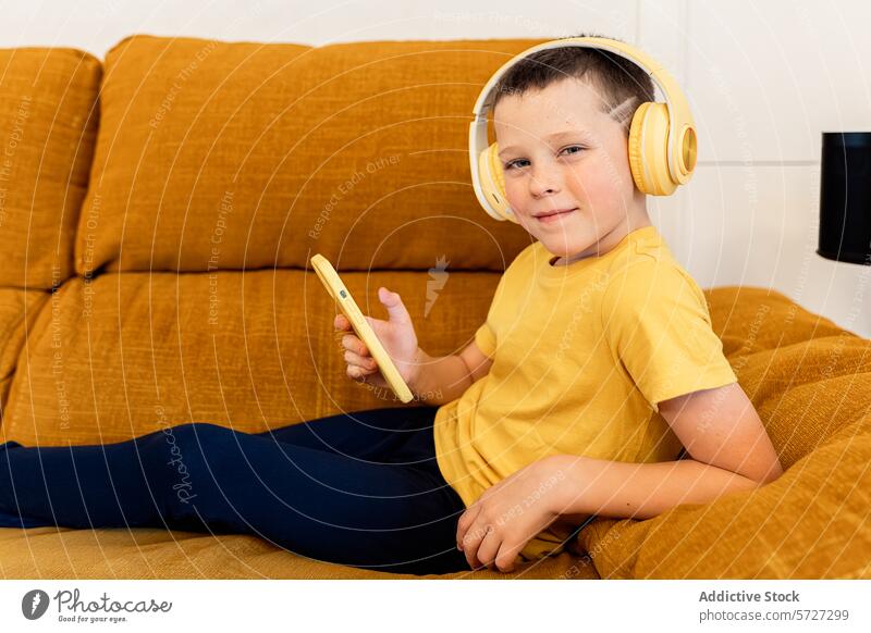 Kleiner Junge genießt zu Hause Musik auf einem Tablet Kind Kopfhörer Tablette Sofa heimwärts Freizeit Technik & Technologie heiter faulenzen Senf gelb
